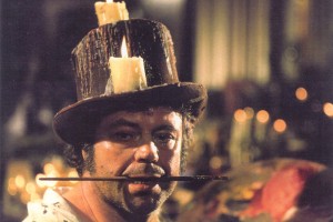 a man wearing a old top hat with candles holding a paint brush in his mouth