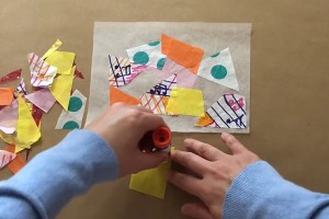 Overhead shot of two hands adding glue to a piece of paper to place onto a collage