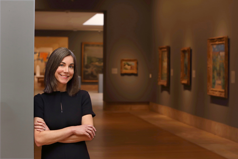 Chief Curator Emily Talbot standing against a gallery wall with her arms folded in front of her body
