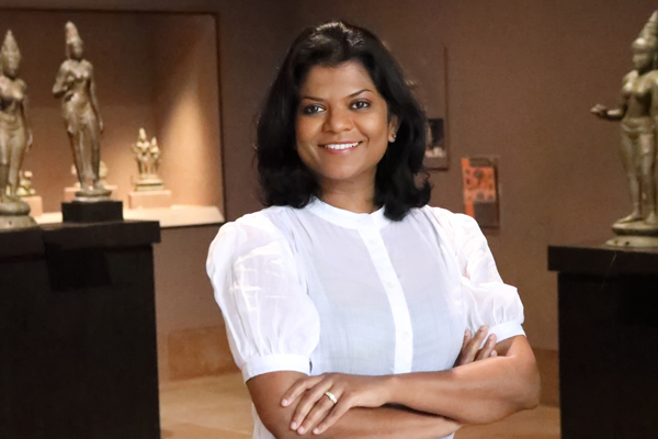 Assistant Curator Lakshika Senarath Gamage posed with her arms folder standing in the center of an Asian art gallery with a white blouse and black pants