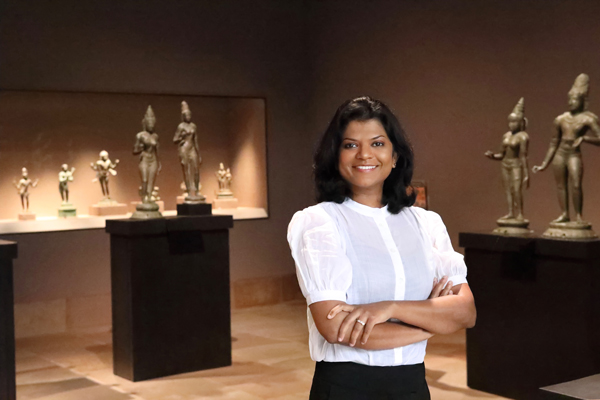 Assistant Curator Lakshika Senarath Gamage posed with her arms folder standing in the center of an asian art gallery with a white blouse and black pants