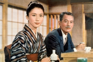 a woman in a kimono and a man in a suit sit in a restaurant