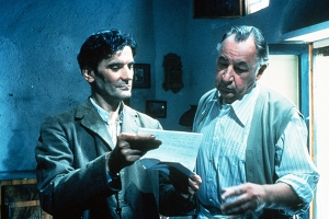 a younger man holds up a letter as an older man reads it