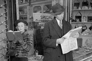 a man and a woman separately read a newspaper while outside a storefront