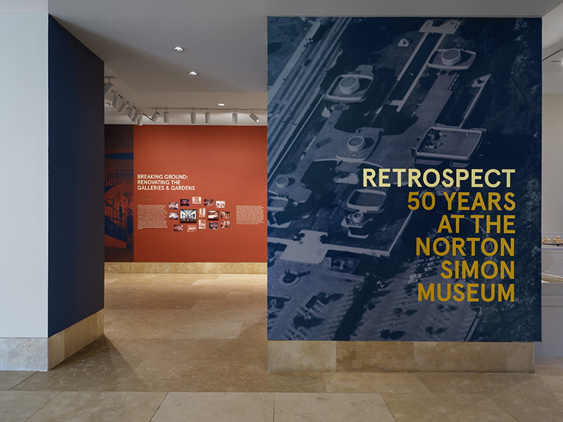 Entrance to a gallery with a photo mural of an archival overhead photo of a building with the text Retrospect 50 Years at the Norton Simon Museum overlaid